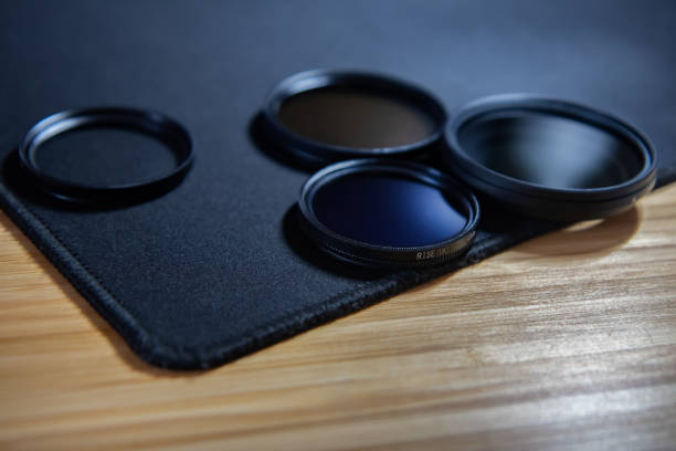 Set of camera lens filters, UV filter, 2 polarized filters and a neutral variable filter, on a black fabric standing on a wooden table.